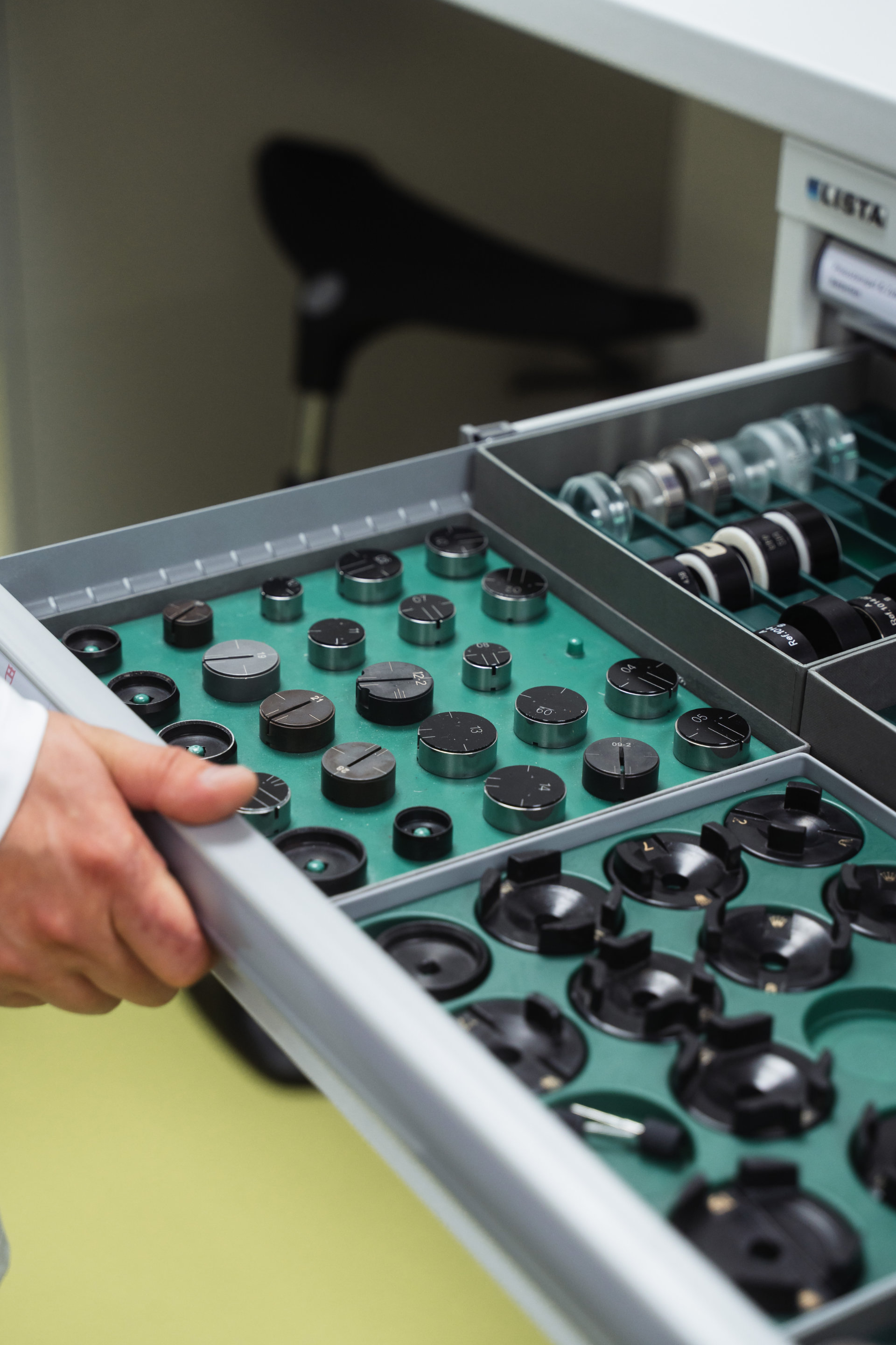 A close-up view of a partially-opened storage drawer filled with precision watch equipment, arranged neatly in individual compartments.