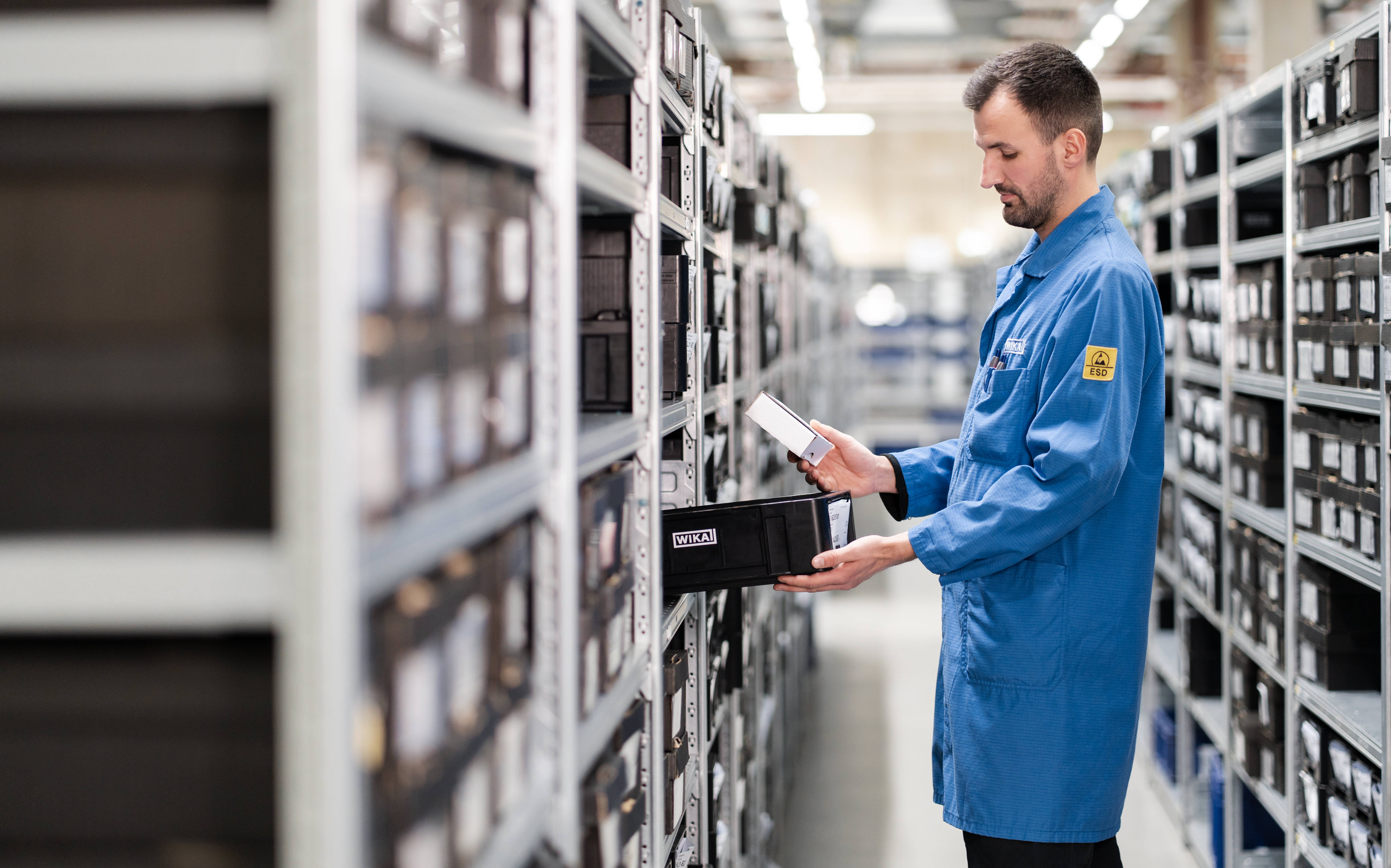 A worker in a blue uniform meticulously checking inventory in a well-organized warehouse.