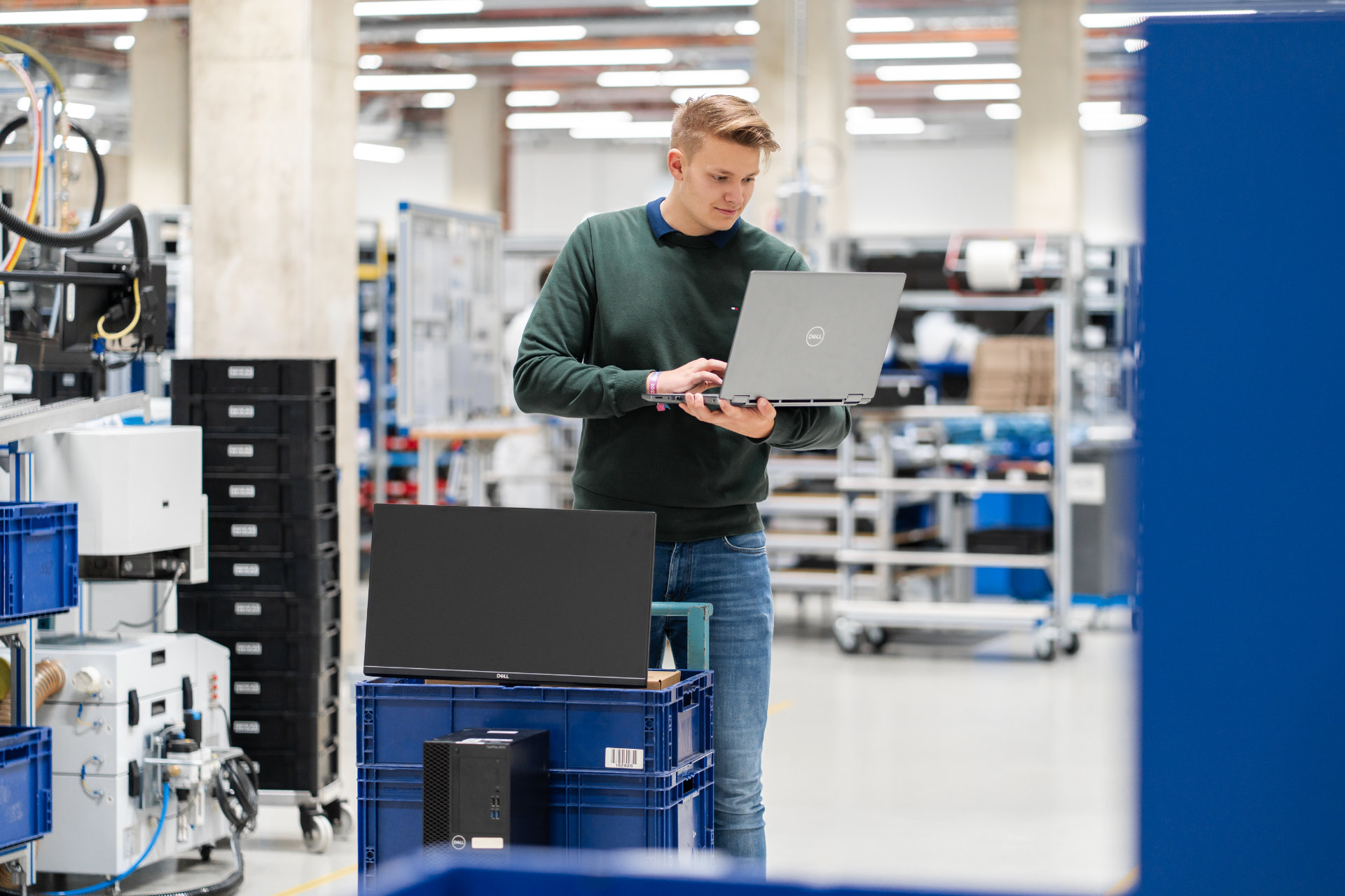 A focused technician using a laptop while standing in a modern industrial facility.
