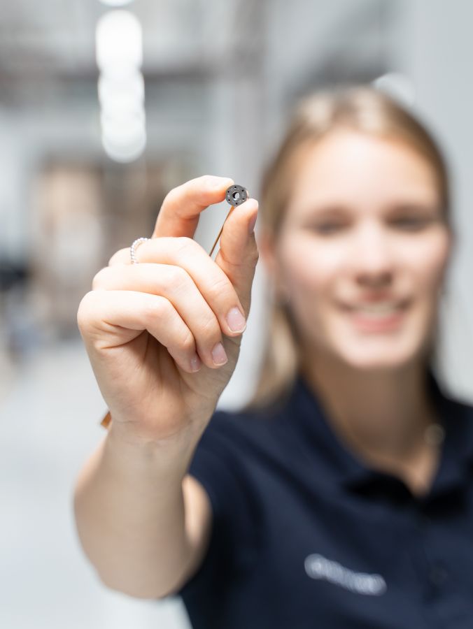A smiling woman presenting a small technological device to the camera with focus on the object in her hand.