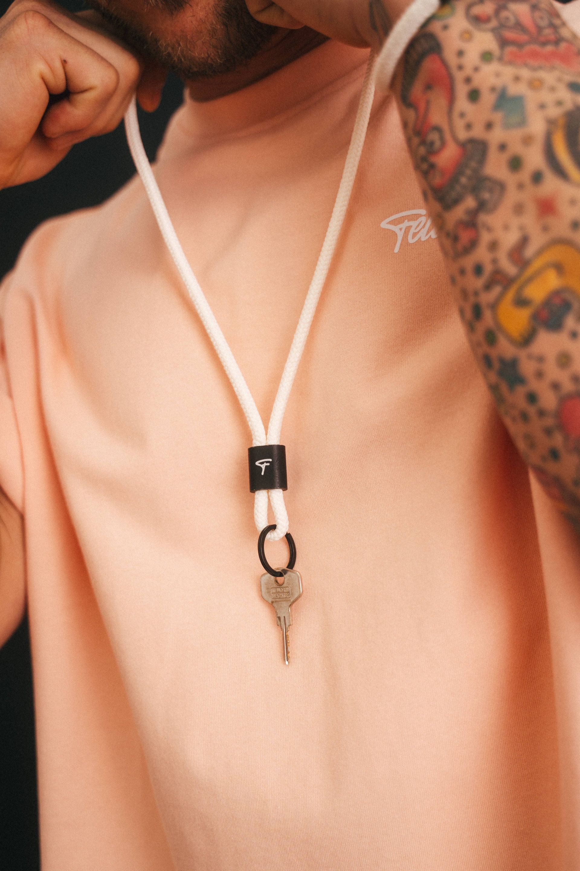 A person with tattooed arms, wearing a pastel-coloured shirt, holding a pipe in his mouth and hanging a key from a ribbon around his neck, perfectly photographed by an Aschaffenburg photographer