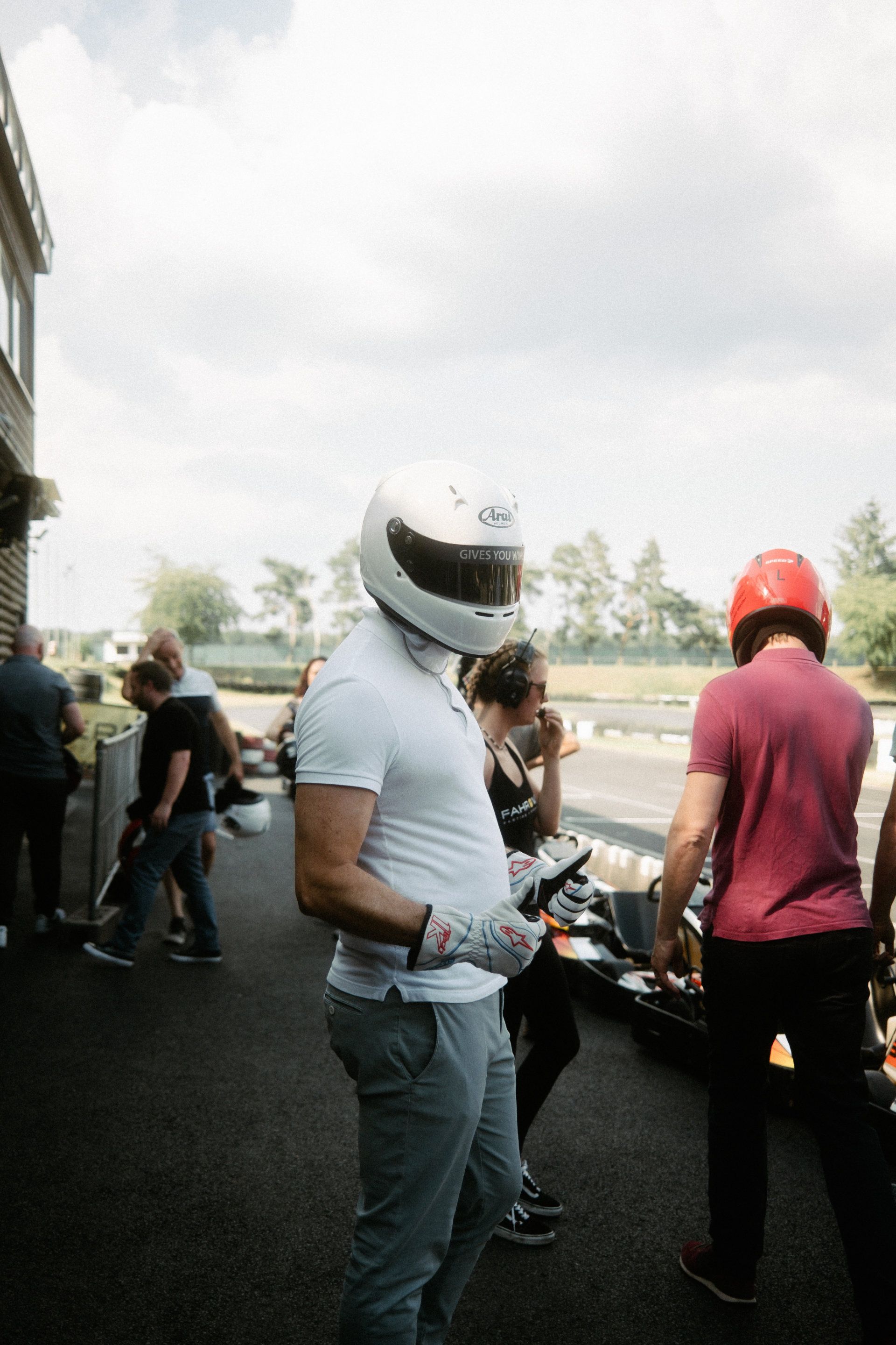 A driver in a white helmet and race gloves awaits the start of a go-kart race, anticipation and focus palpable in the air, an ideal scene for event photography.