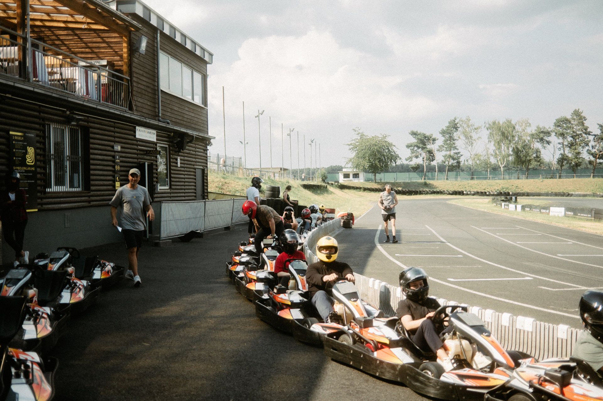 A lineup of go-karts and drivers ready for a race, with a bustling track environment in the background, captured by a videographer specializing in event photography.