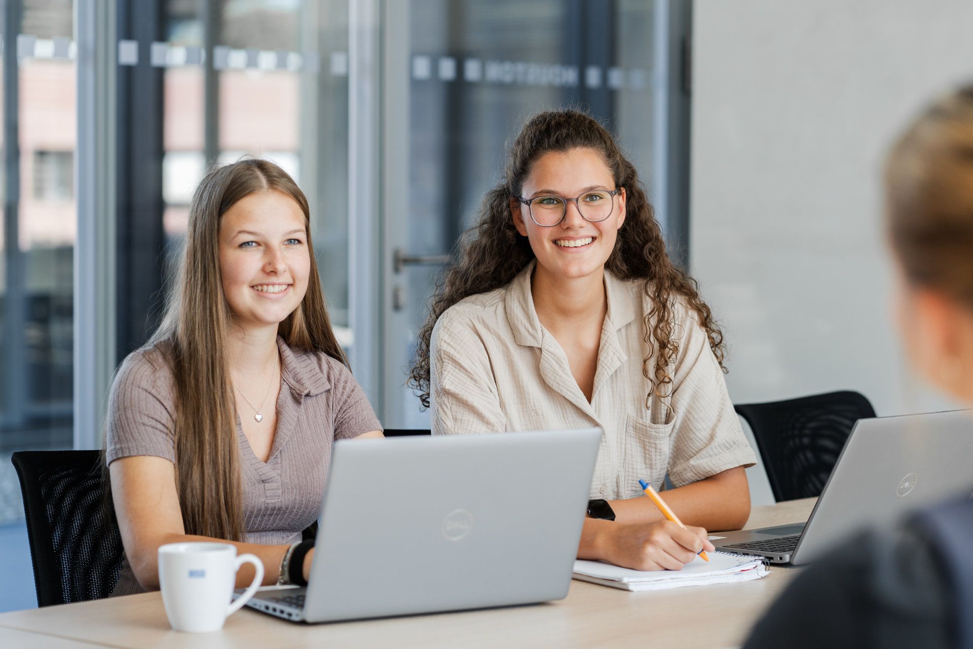 Two smiling professional women engaging in a collaborative work session at a conference table with laptops and notebooks, exuding a friendly and productive atmosphere, captured beautifully by Alexander Möller.