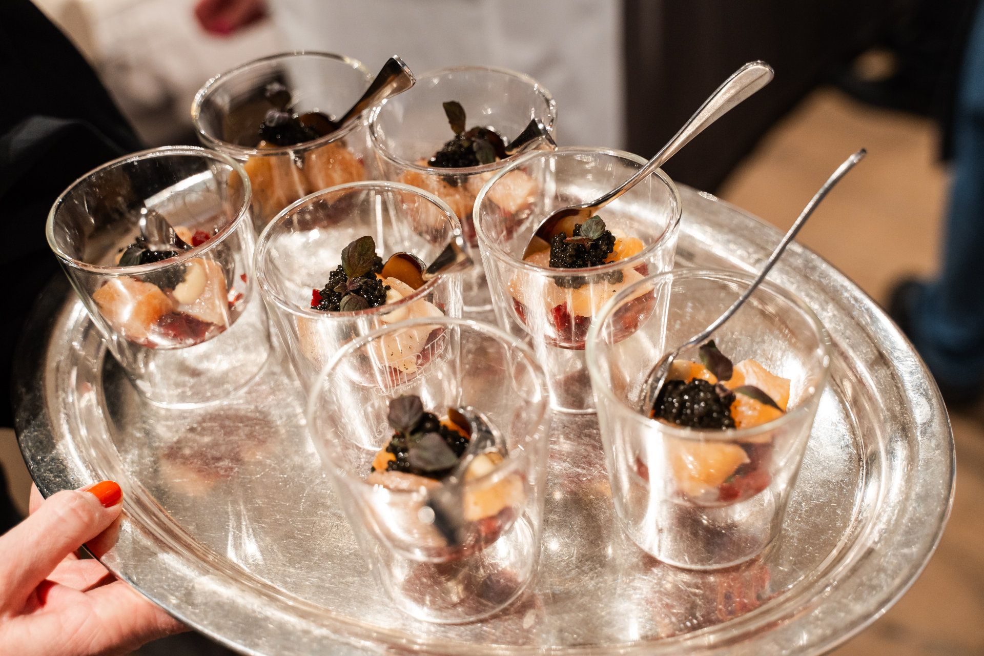 A server's hand holding a tray of elegant appetizers in clear glasses garnished with black toppings, ready to be enjoyed at a sophisticated event captured by an Aschaffenburg photographer.