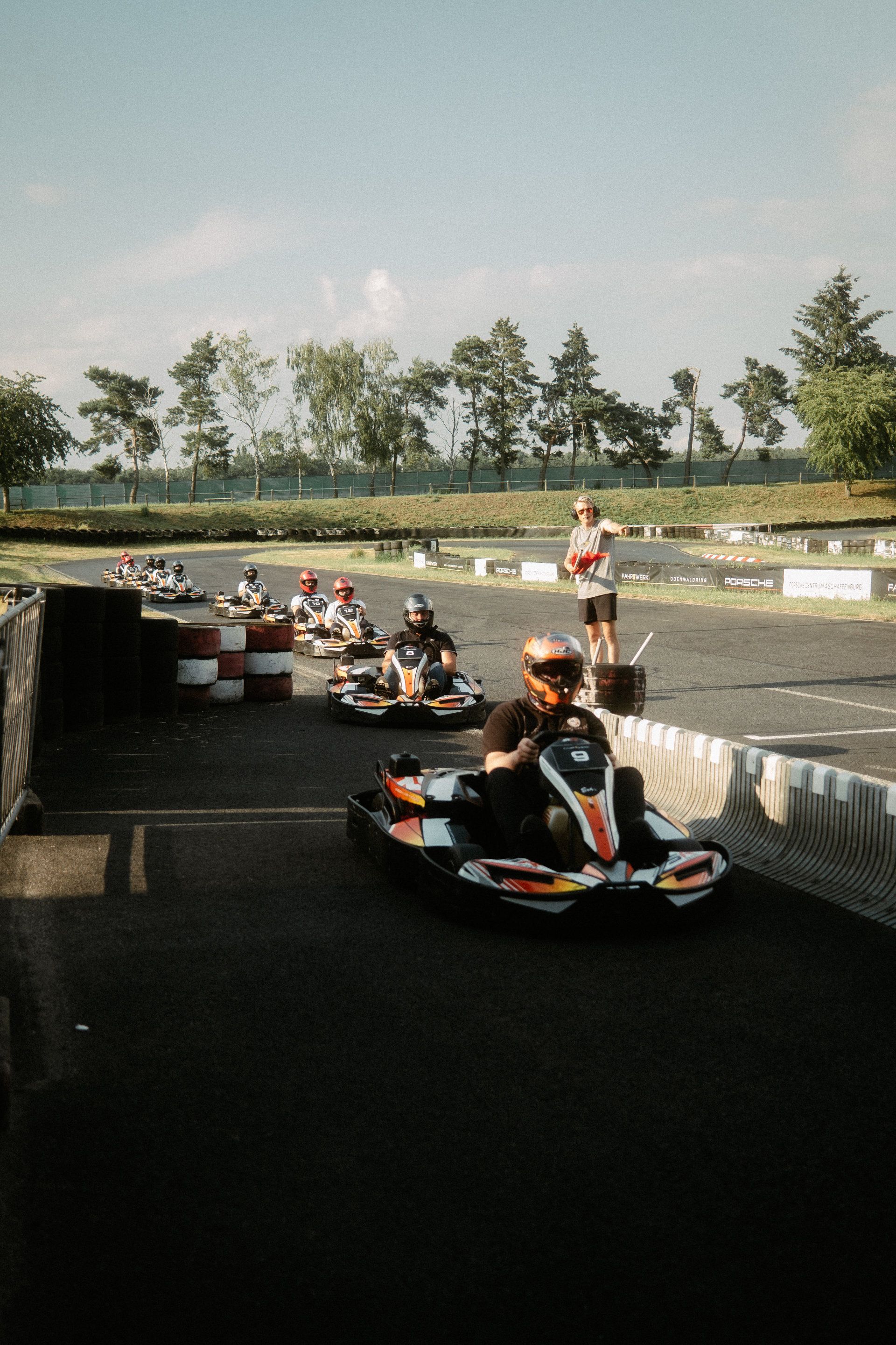 A group of go-kart racers lined up at the starting line, ready to accelerate into an exciting race on a sunny day, as a photographer from Aschaffenburg watches on.