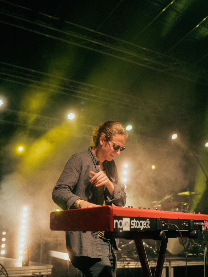A musician lost in the moment while playing a red keyboard on stage, bathed in the atmospheric glow of stage lights and a haze of performance fog, captured brilliantly by an Aschaffenburg photographer.